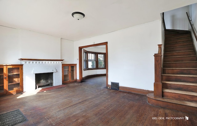 unfurnished living room with baseboards, visible vents, hardwood / wood-style flooring, stairs, and a brick fireplace