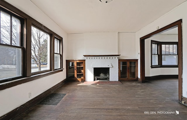 unfurnished living room with a fireplace, wood finished floors, visible vents, and baseboards