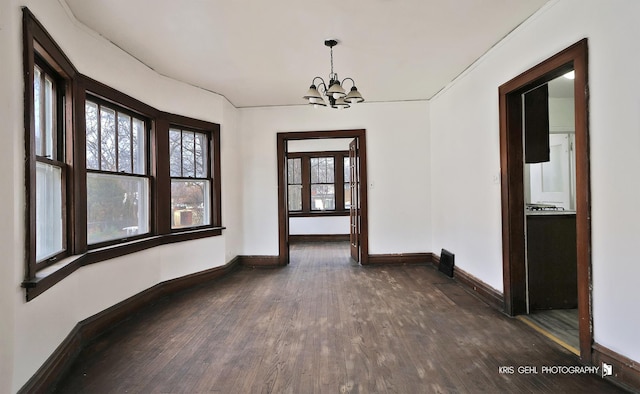 spare room with a notable chandelier, dark wood finished floors, and baseboards