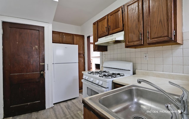 kitchen featuring tasteful backsplash, light countertops, a sink, white appliances, and under cabinet range hood