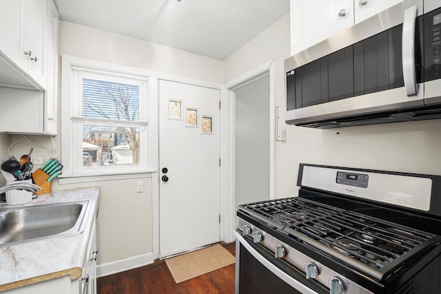 kitchen featuring white cabinets, appliances with stainless steel finishes, dark wood-type flooring, light countertops, and a sink