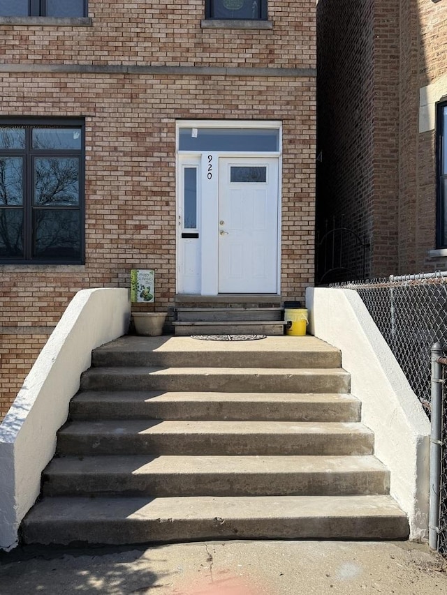 view of exterior entry with fence and brick siding