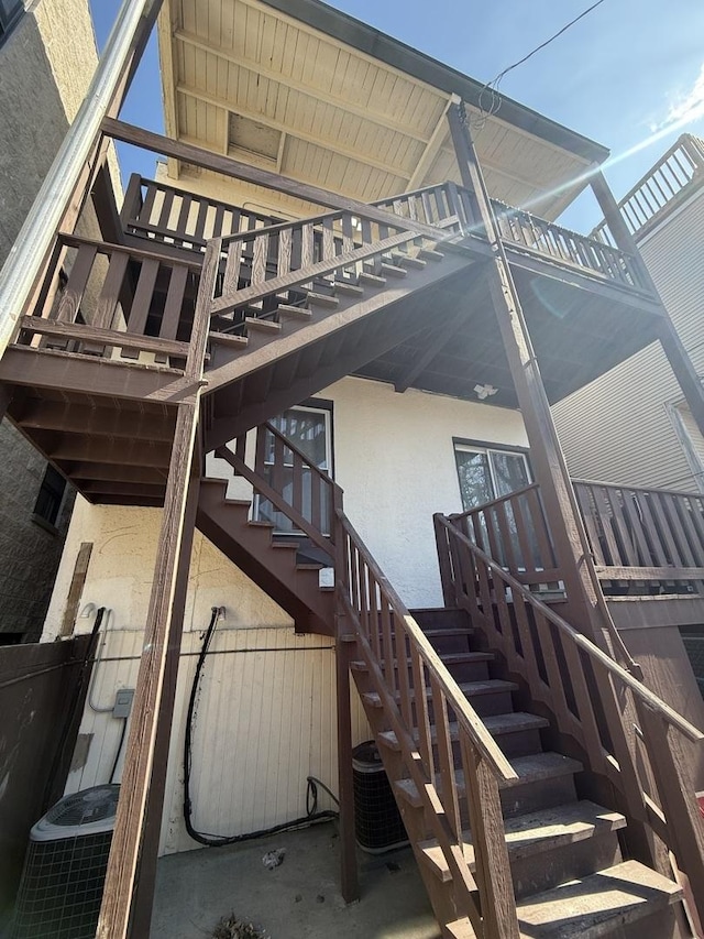 rear view of house with stairs, central AC unit, and stucco siding