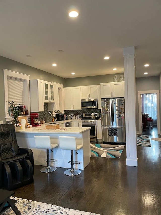 kitchen featuring stainless steel appliances, dark wood-type flooring, a peninsula, white cabinets, and decorative columns