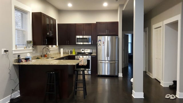 kitchen featuring light stone counters, a breakfast bar area, a peninsula, stainless steel appliances, and a sink