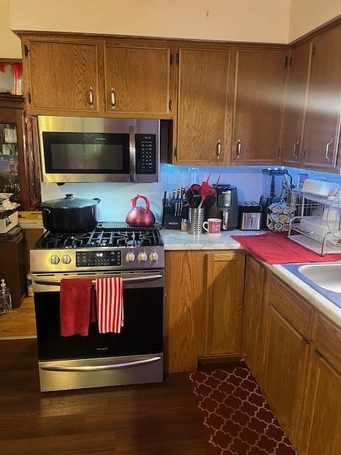 kitchen with dark wood finished floors, brown cabinetry, appliances with stainless steel finishes, and light countertops