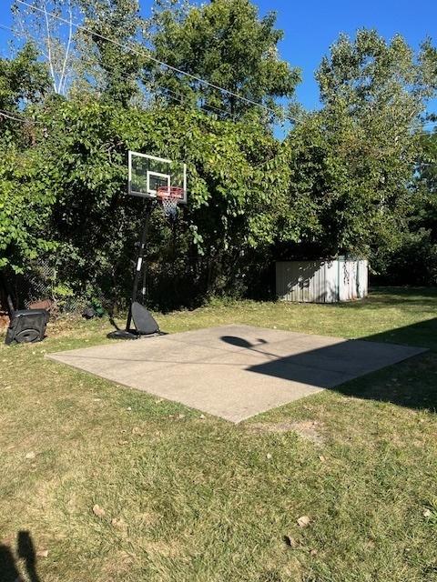 view of sport court featuring basketball hoop and a lawn