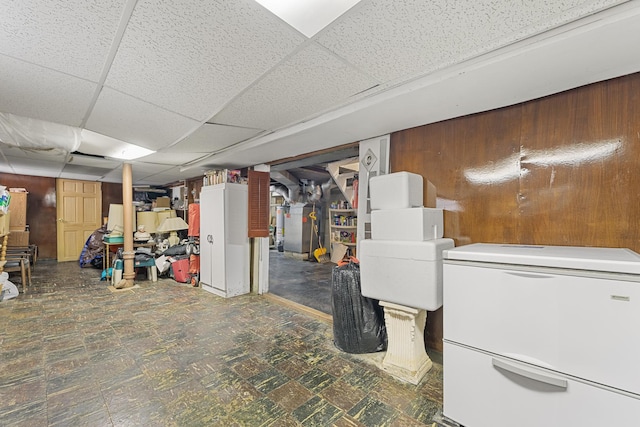 finished below grade area featuring a paneled ceiling, fridge, wooden walls, and tile patterned floors