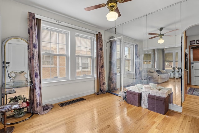 interior space with arched walkways, visible vents, a ceiling fan, wood finished floors, and baseboards