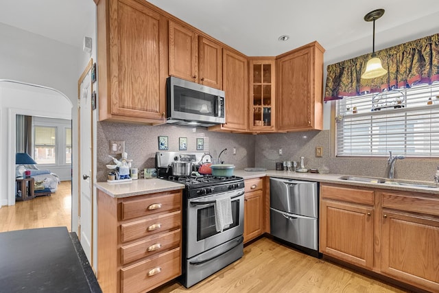 kitchen featuring light wood-style flooring, a sink, appliances with stainless steel finishes, tasteful backsplash, and glass insert cabinets