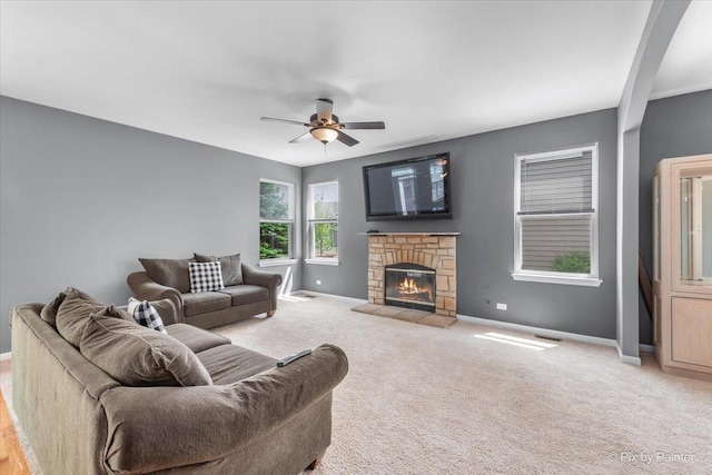 living room featuring a stone fireplace, carpet, a ceiling fan, and baseboards