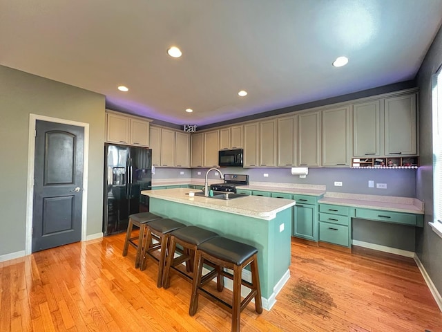 kitchen featuring light countertops, light wood-style flooring, a sink, black appliances, and a kitchen breakfast bar