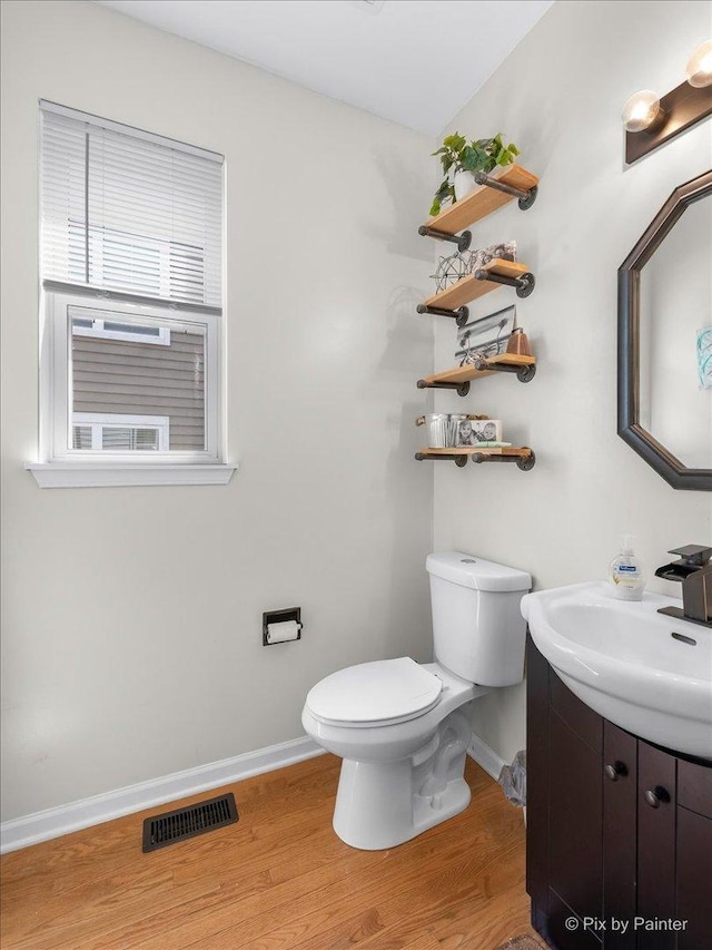 half bathroom with visible vents, toilet, vanity, wood finished floors, and baseboards