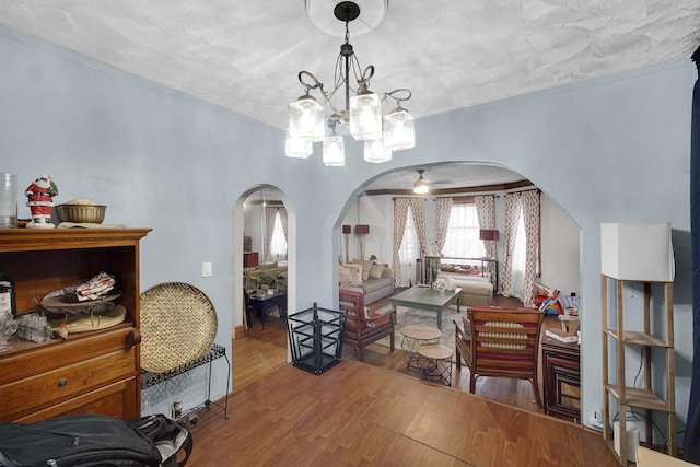 dining area with arched walkways, ceiling fan with notable chandelier, ornamental molding, and wood finished floors