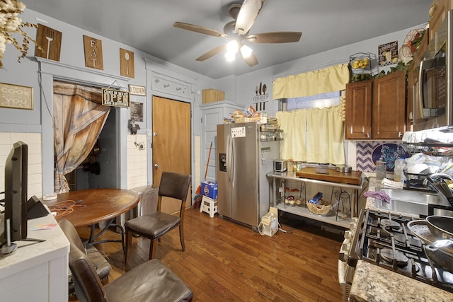 kitchen featuring dark wood-type flooring, brown cabinetry, a ceiling fan, and appliances with stainless steel finishes