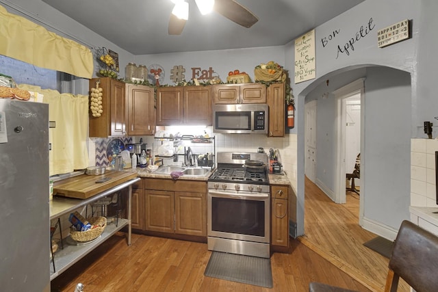 kitchen with arched walkways, brown cabinets, stainless steel appliances, and a sink