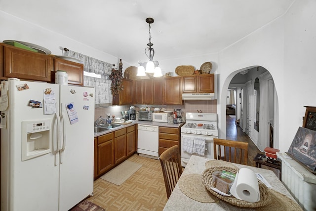 kitchen with under cabinet range hood, a sink, white appliances, arched walkways, and decorative backsplash