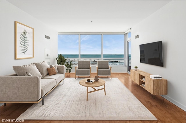 living room featuring a wall of windows, baseboards, wood finished floors, and visible vents