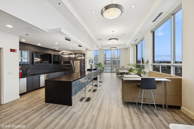 kitchen with stainless steel appliances, pendant lighting, light wood-style floors, a breakfast bar area, and dark countertops