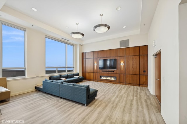 living room featuring light wood finished floors, visible vents, a raised ceiling, and baseboards