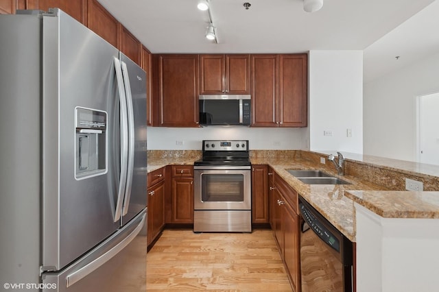 kitchen with light stone countertops, light wood-type flooring, stainless steel appliances, a peninsula, and a sink