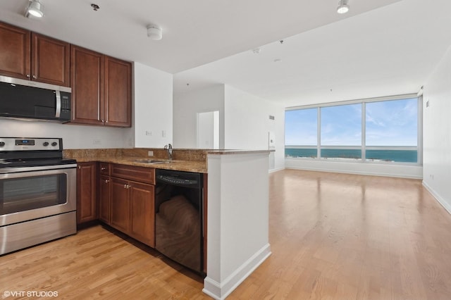 kitchen with light wood-style flooring, stainless steel appliances, a peninsula, a water view, and a sink