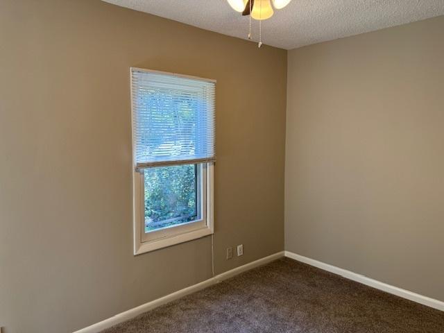 spare room with a textured ceiling and dark carpet