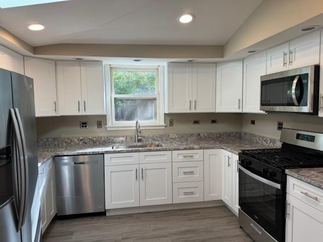 kitchen with appliances with stainless steel finishes, light stone counters, lofted ceiling, sink, and white cabinetry