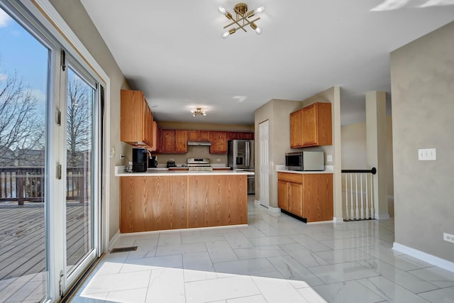 kitchen with under cabinet range hood, appliances with stainless steel finishes, a peninsula, light countertops, and baseboards