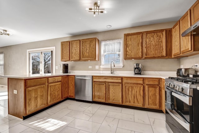 kitchen with marble finish floor, a sink, appliances with stainless steel finishes, a peninsula, and light countertops