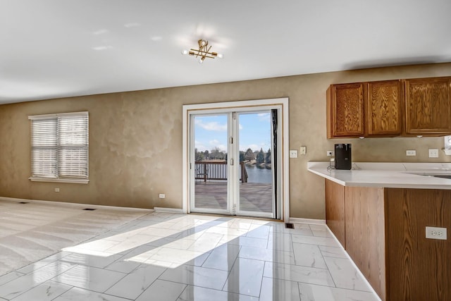 kitchen featuring baseboards, brown cabinets, marble finish floor, and light countertops