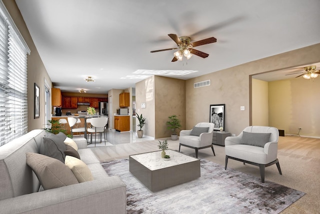 living area with visible vents, baseboards, light colored carpet, and ceiling fan