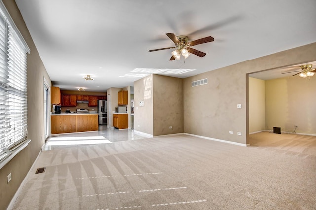 unfurnished living room with light carpet, visible vents, baseboards, and a ceiling fan