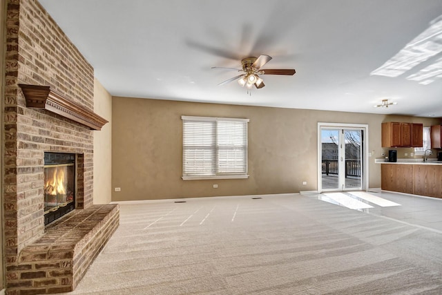 unfurnished living room featuring a brick fireplace, baseboards, light colored carpet, a ceiling fan, and a sink