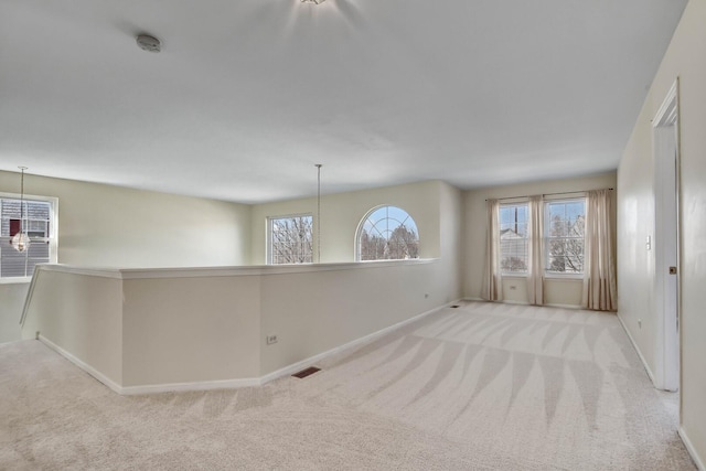 carpeted spare room featuring an inviting chandelier, a healthy amount of sunlight, and visible vents