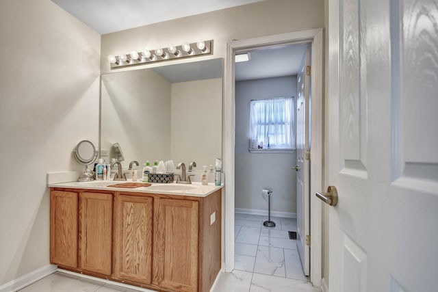 bathroom featuring double vanity, marble finish floor, baseboards, and a sink