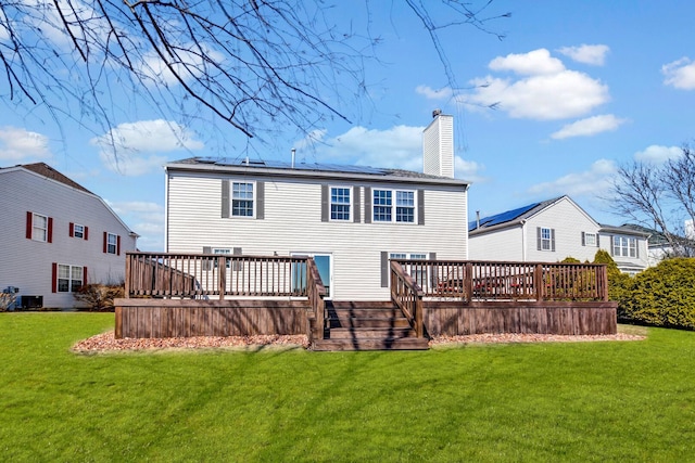 rear view of property featuring solar panels, a wooden deck, central AC unit, a chimney, and a yard