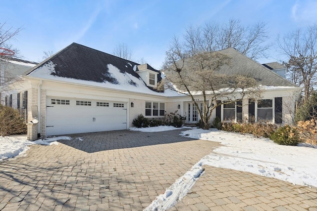 view of front of house with decorative driveway, brick siding, an attached garage, and roof with shingles