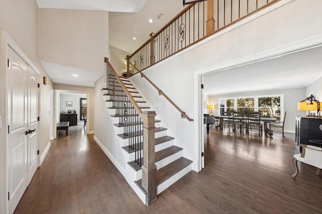 staircase featuring a high ceiling, baseboards, and wood finished floors