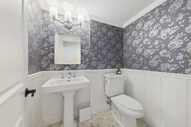 bathroom with wainscoting, a sink, toilet, and wallpapered walls