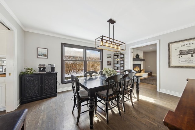 dining room with ornamental molding, dark wood-style flooring, a fireplace, and baseboards