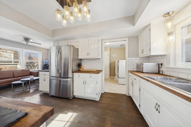 kitchen with white cabinets, white microwave, butcher block counters, decorative light fixtures, and freestanding refrigerator