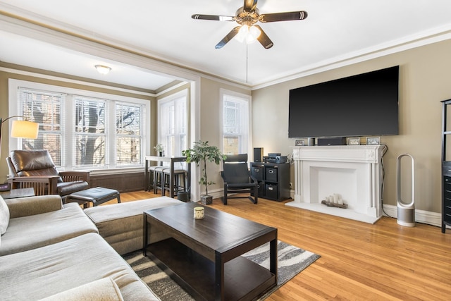 living room featuring a ceiling fan, crown molding, baseboards, and wood finished floors