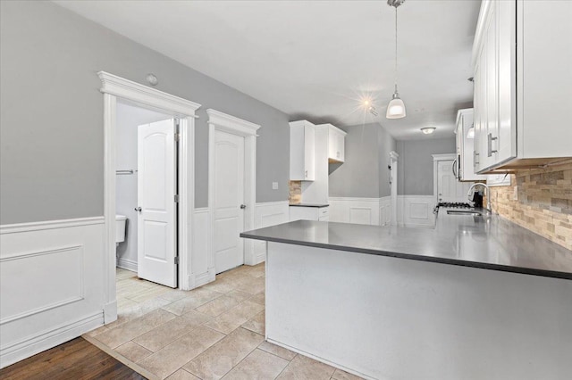 kitchen featuring wainscoting, a sink, white cabinetry, and pendant lighting