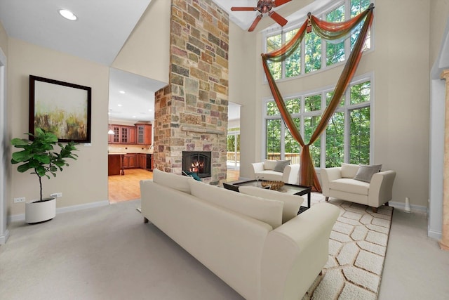 carpeted living room featuring a fireplace, ceiling fan, a towering ceiling, and a healthy amount of sunlight