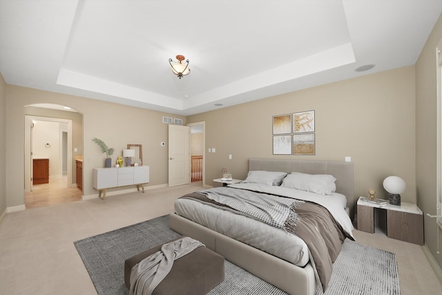 bedroom featuring light carpet, connected bathroom, and a raised ceiling