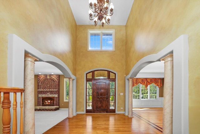 foyer entrance featuring a high ceiling, ornate columns, a brick fireplace, and wood-type flooring