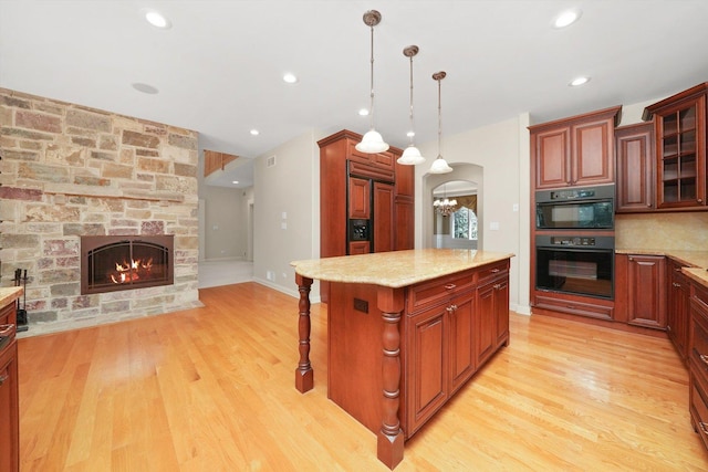 kitchen featuring double oven, a breakfast bar, light stone counters, a center island, and hanging light fixtures