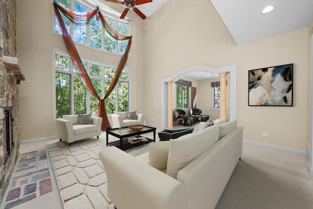 carpeted living room featuring a fireplace, high vaulted ceiling, ornate columns, and ceiling fan