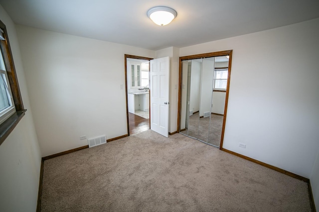 unfurnished bedroom featuring baseboards, visible vents, a closet, and light colored carpet